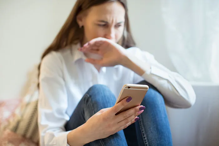 Worried woman sitting indoors looking at her phone, reflecting on emotional moments healthcare workers face.