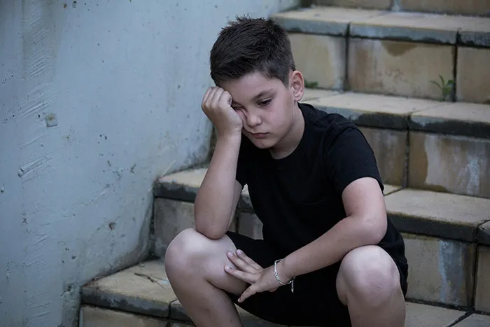 Sad young boy sitting alone on outdoor stairs, reflecting the impact of parents who disowned their children.