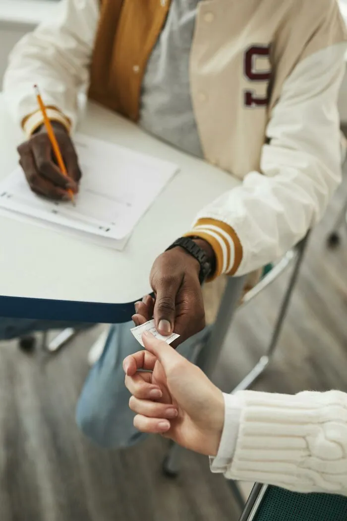 Two students exchanging a small paper note during a test, capturing moments of unique childhood joys before smartphones.