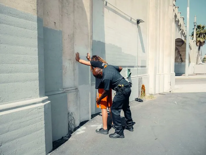 Policía registrando a una persona contra una pared en una calle, mostrando una escena de conversaciones privadas terroríficas.