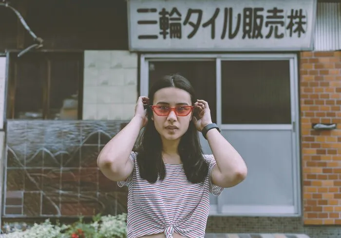 Young woman wearing red sunglasses outside a Japanese building, illustrating foreigners big in Japan experiences.