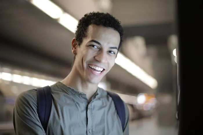 Smiling young man with curly hair and backpack, showcasing really good genes in a bright, modern setting.
