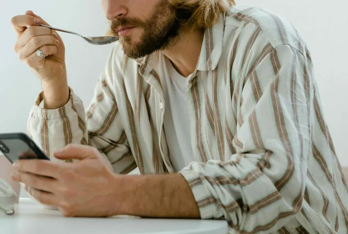 A man in a striped shirt eating with a spoon while looking at his phone, illustrating insane hospital experiences.