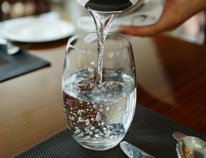Glass being filled with water at a restaurant table, illustrating Americans reveal things non-Americans do like breaking spaghetti.