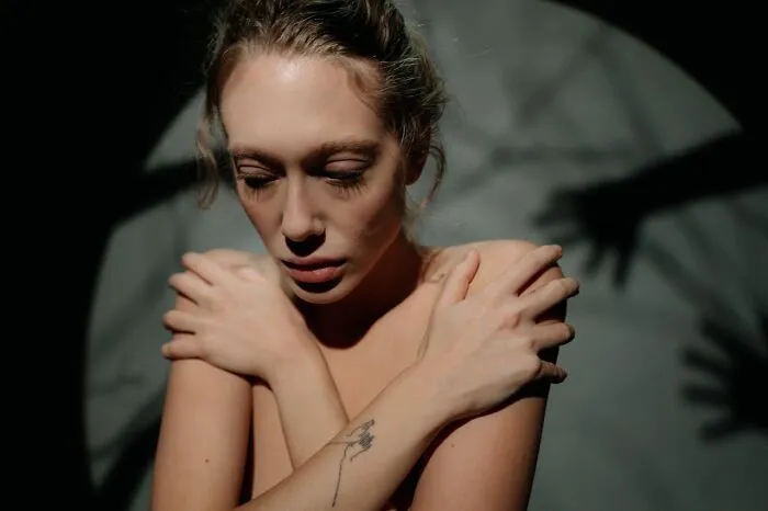 Woman with closed eyes hugging herself in a dark room with eerie shadows, reflecting an insane hospital experience.