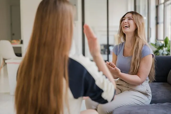 Two young women laughing and playing hand games indoors, capturing childhood joys before smartphones changed experiences.