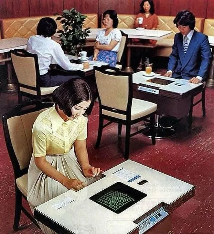 Mujeres y hombre en cafetería con mesas de videojuego vintage, mostrando un lado distinto de la historia tecnológica.