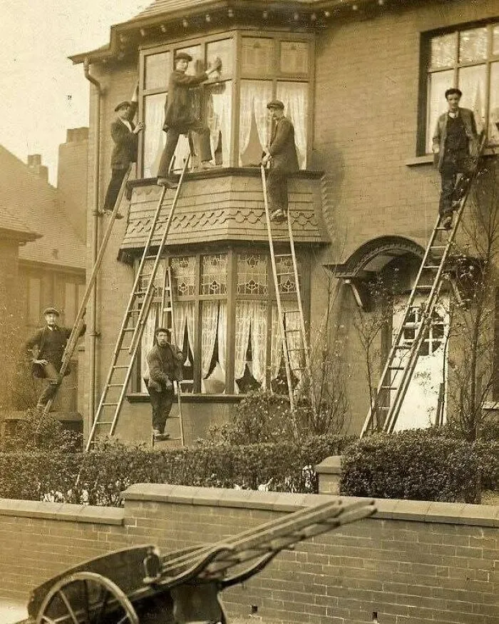 Hombres en escaleras limpiando ventanas de una casa antigua mostrando un lado distinto de la historia.