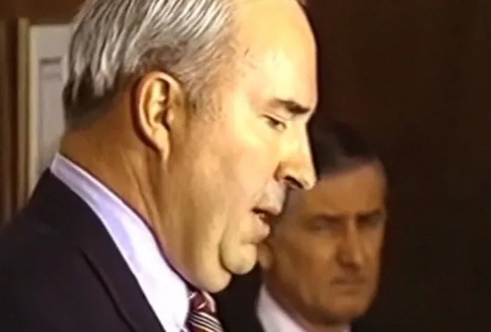 Two men in suits captured in a candid moment during a shocking live television event from Gen X era.