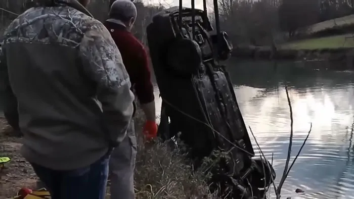 Two men by a riverbank watching a car being pulled out of water, capturing shocking moments on live television.