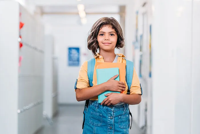 Young girl in a school hallway holding books, representing kids' lies that started off silly and got way too real.