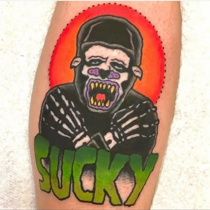 Tattoo of a roaring gorilla with a red background and green text saying SUCKY, showcasing bizarre tattoo choices.