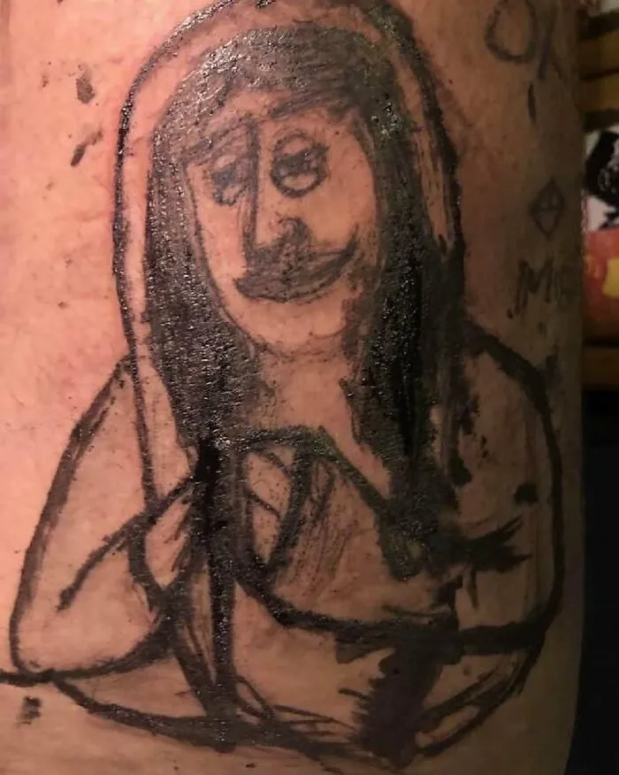 Close-up of a bizarre tattoo featuring an abstract, rough sketch of a person with long hair and a mustache on skin.