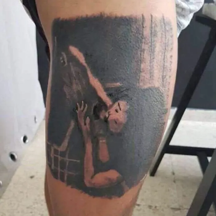 Tattoo on leg showing a distorted and bizarre tattoo choice featuring a person embracing a figure in dark tones.