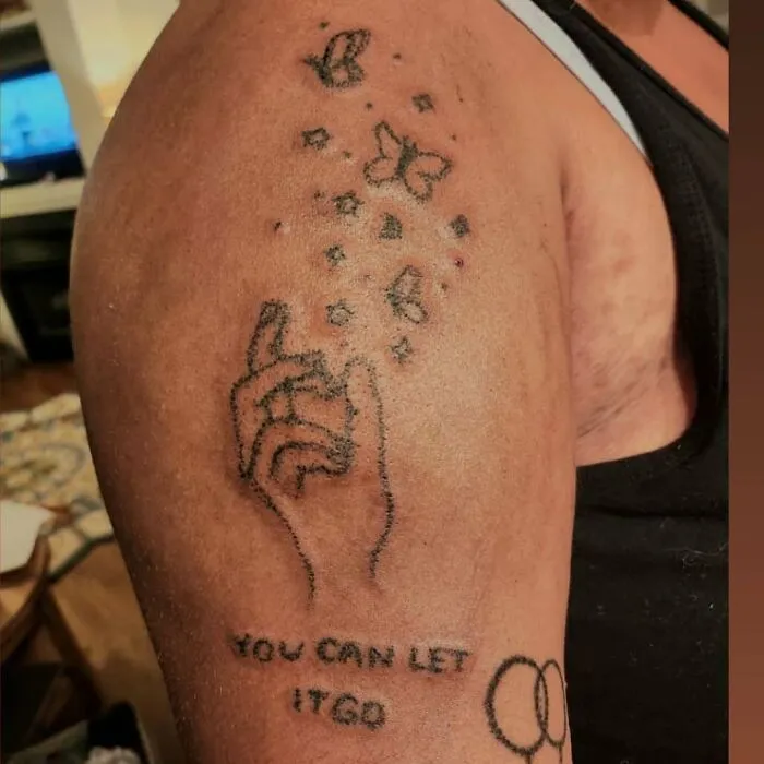 Close-up of a bizarre tattoo choice showing a hand with butterflies and the phrase you can let it go on an arm.