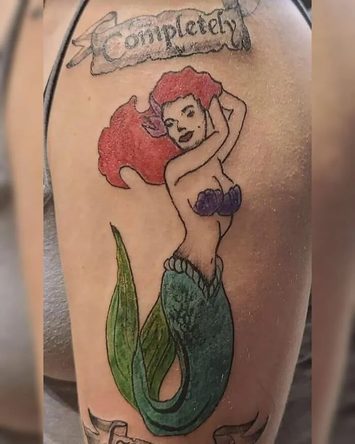 Mermaid tattoo with red hair and purple shell top on arm, showcasing bizarre choices people made while getting tattoos.