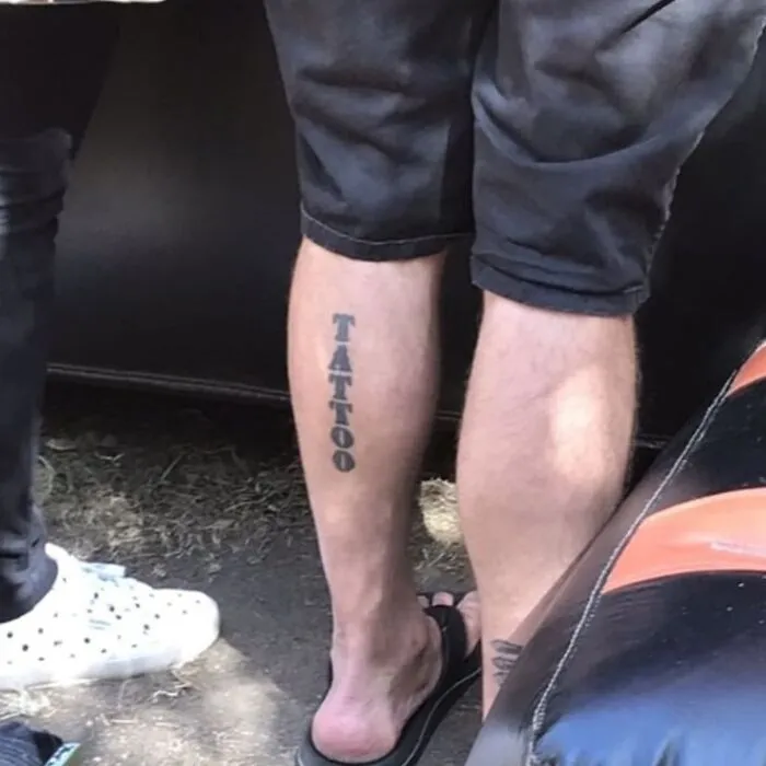 Leg tattoo with the word tattoo inked vertically in bold black letters, a bizarre tattoo choice among others.