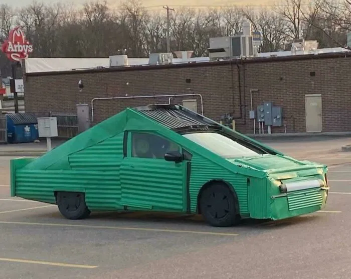Green car with an outrageous custom corrugated metal exterior parked in a lot showing extreme car mods.