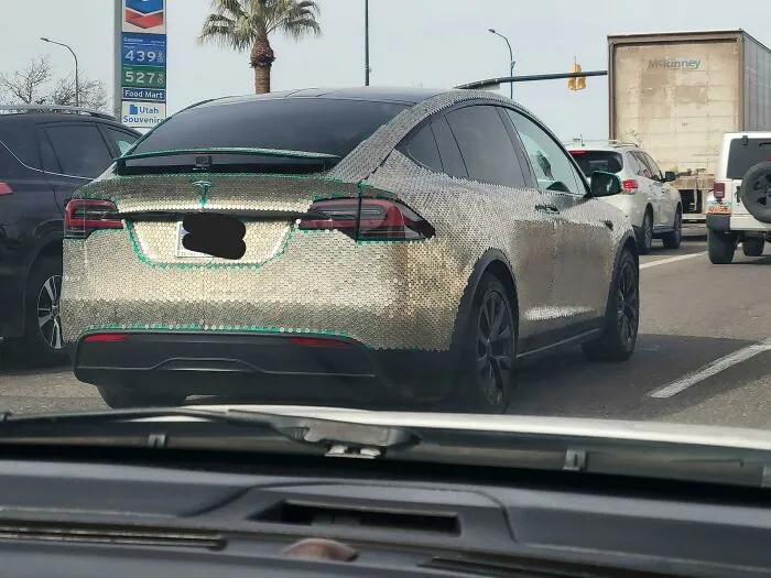 Electric car fully covered with shiny metallic scales modification on a city street, an outrageous car mod seen in traffic.