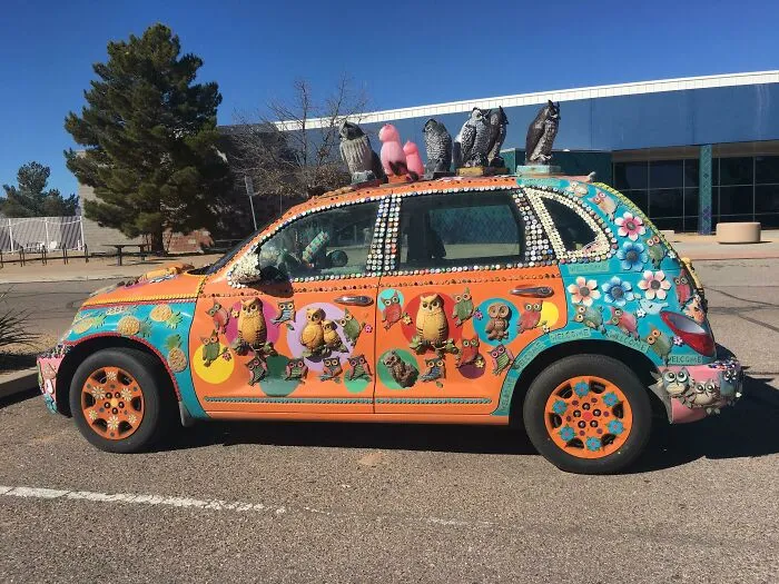 Brightly painted car with owl sculptures and decorative embellishments showcasing outrageous car mods on a sunny day.