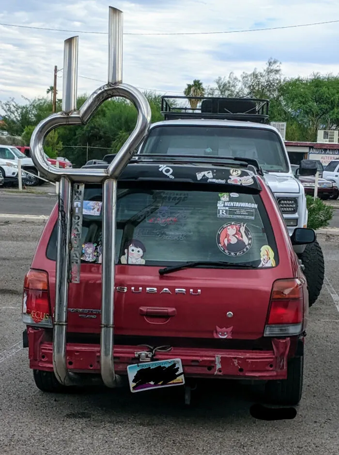 Red Subaru with outrageous car mods including a large heart-shaped dual exhaust extending above the roof.