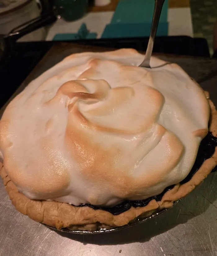 Meringue pie with unevenly browned topping and a fork stuck awkwardly in the dessert, showing clueless partner cooking fail.
