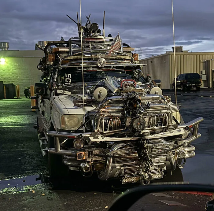 Unique car covered in outrageous car mods with excessive metalwork and accessories parked in an industrial area at dusk