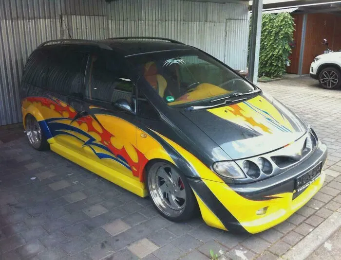 Modified compact car with custom lowered body, vibrant flame decals, and unique multi-headlight design parked in a garage.