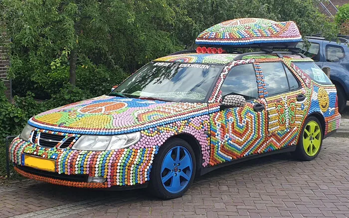 Car covered in colorful bottle cap mods with mismatched blue and yellow wheels, showcasing an outrageous car mod design.