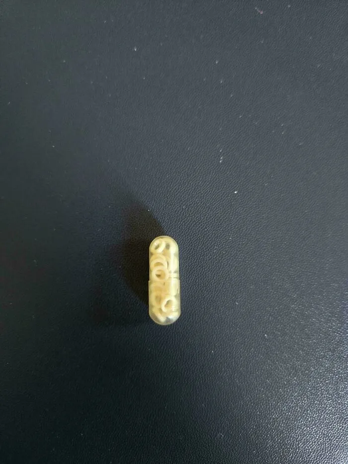 Capsule filled with tiny alphabet-shaped pasta on a dark surface, seen in a mildly interesting way.