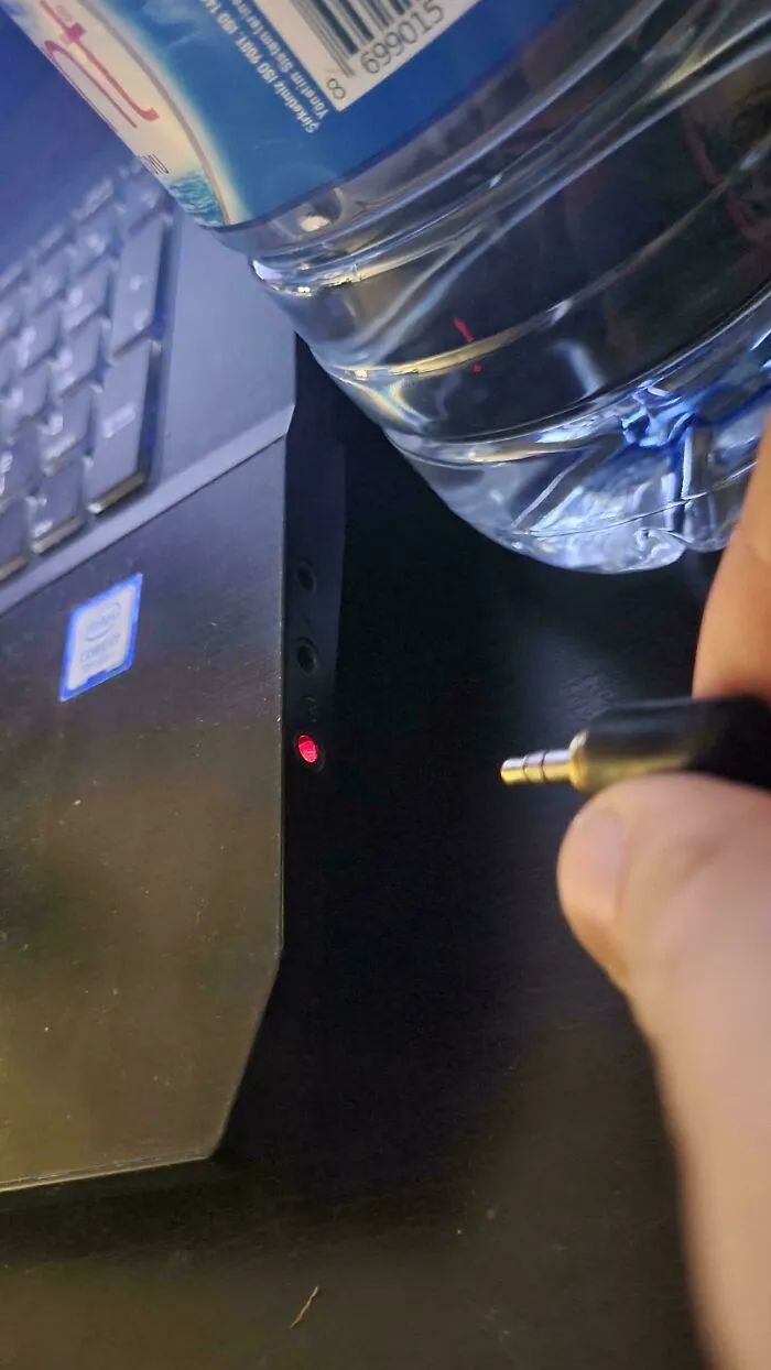 Close-up of a headphone jack next to a laptop with a water bottle reflecting light, showing a mildly interesting moment.