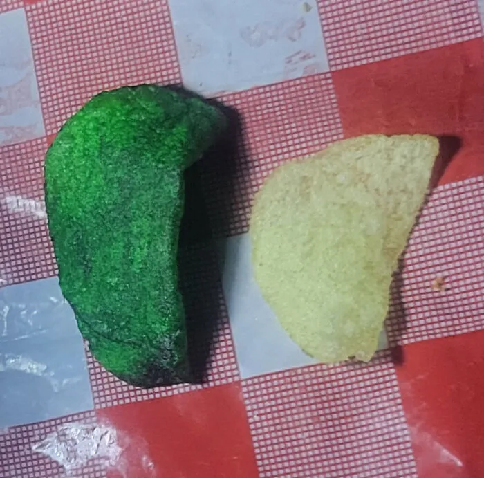 Two potato chips on a red and white checkered surface, one unusually green, capturing mildly interesting snack variety.