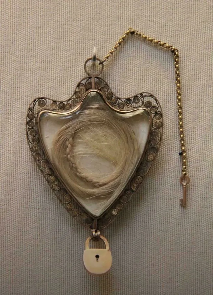 Heart-shaped vintage hair keepsake with ornate metal frame, lock, and key, showcasing mildly interesting historical artifact.