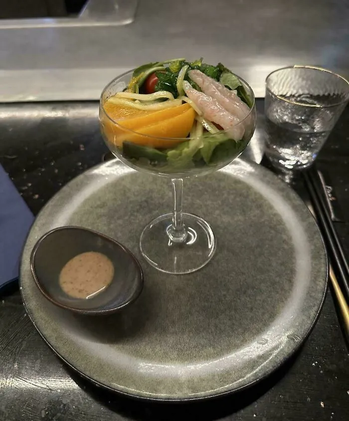 Salad with raw shrimp and fruit served in a cocktail glass with dipping sauce on a plate, an unholy meal presentation.