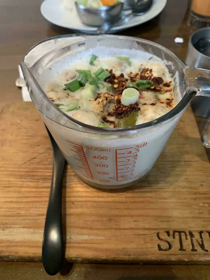 A creamy meal served in a glass measuring cup with green onions and chili flakes, an unholy way to serve food.