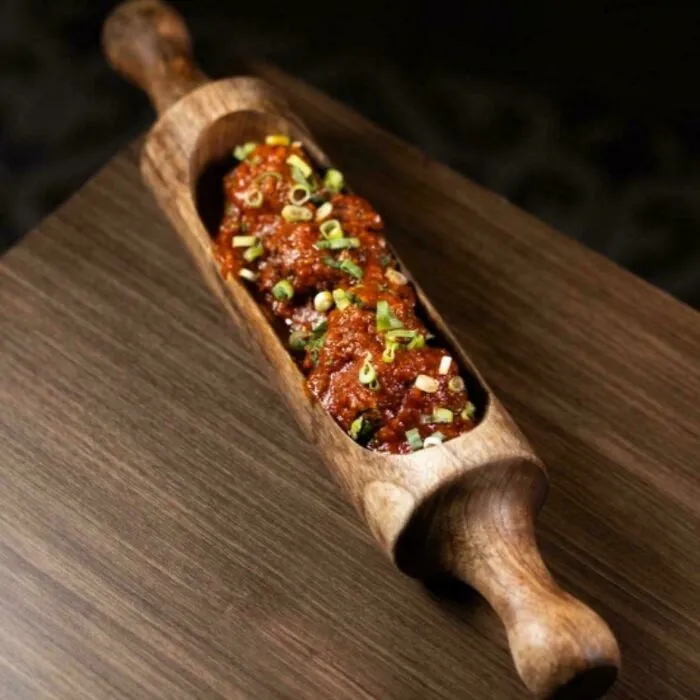 Unholy meal presentation of meatballs served inside a hollow wooden rolling pin, garnished with chopped green onions.