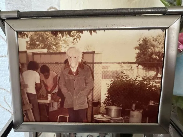 Old photo of a mysterious elderly person standing with hands in pockets in a vintage outdoor setting, intriguing mystery concept.