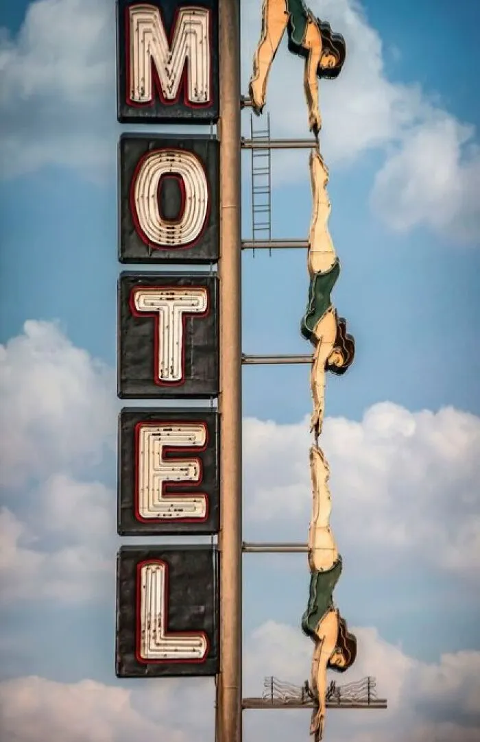 Vintage motel neon sign with acrobatic figures in swimsuits against a cloudy sky, a classic vintage thing.