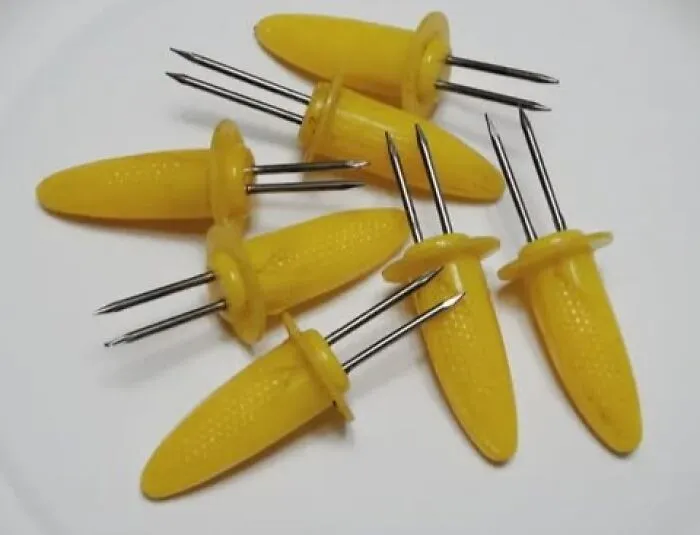 Yellow vintage corn holders with metal prongs arranged on a white surface, showcasing unique vintage things.
