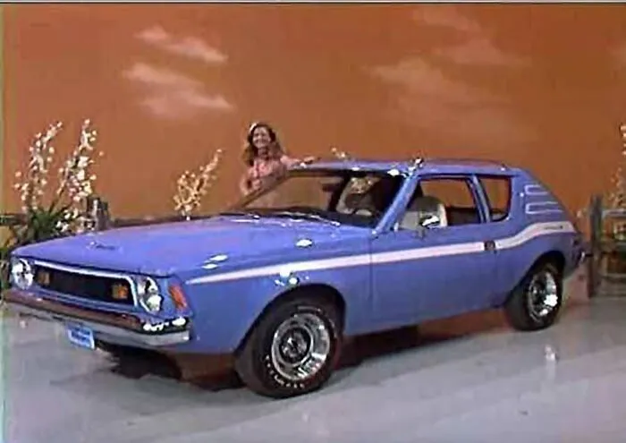 Vintage blue compact car on display indoors with a woman standing behind, showcasing unique vintage things collection.