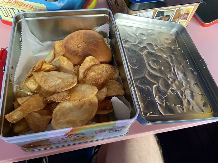 Tin lunchbox containing a burger and potato chips, an example of meals served in unholy ways possible.