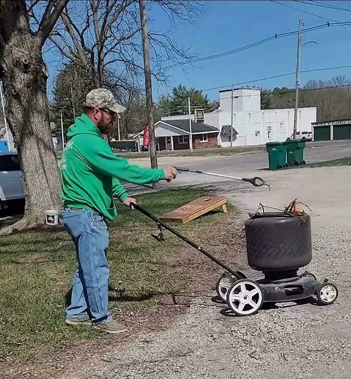 Man using redneck engineering to turn a lawnmower into a portable fire pit outside on a sunny day.
