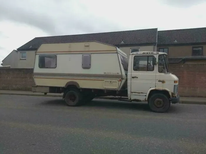 Old truck with a camper creatively attached showcasing redneck engineering and inventive MacGyvering on a residential street.