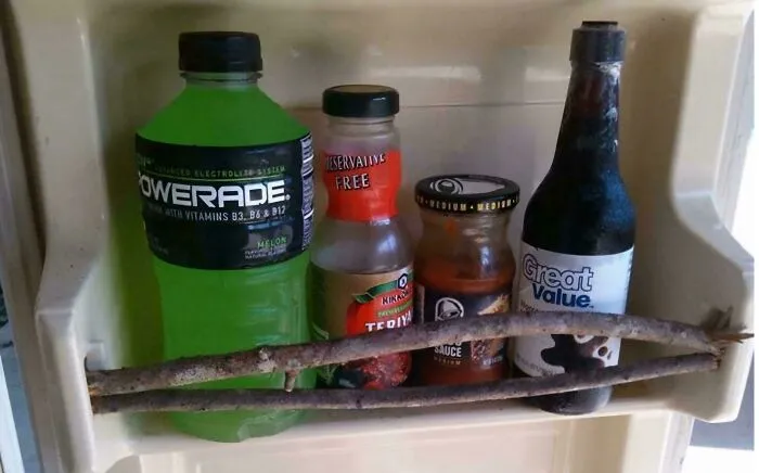 Fridge door secured with sticks as a creative redneck engineering solution to hold bottles in place.