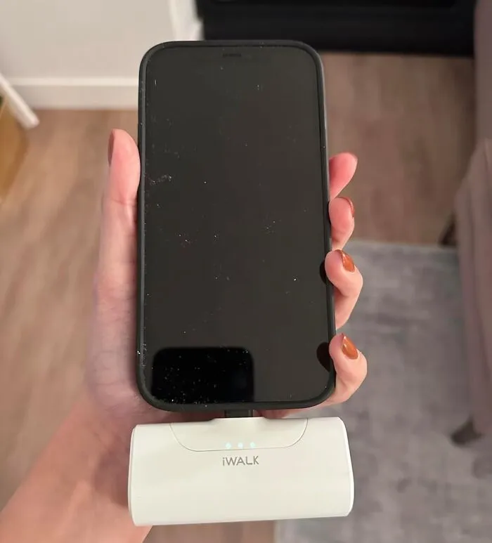 Hand holding smartphone connected to portable charger showing travel essentials for hot girl summer itinerary.