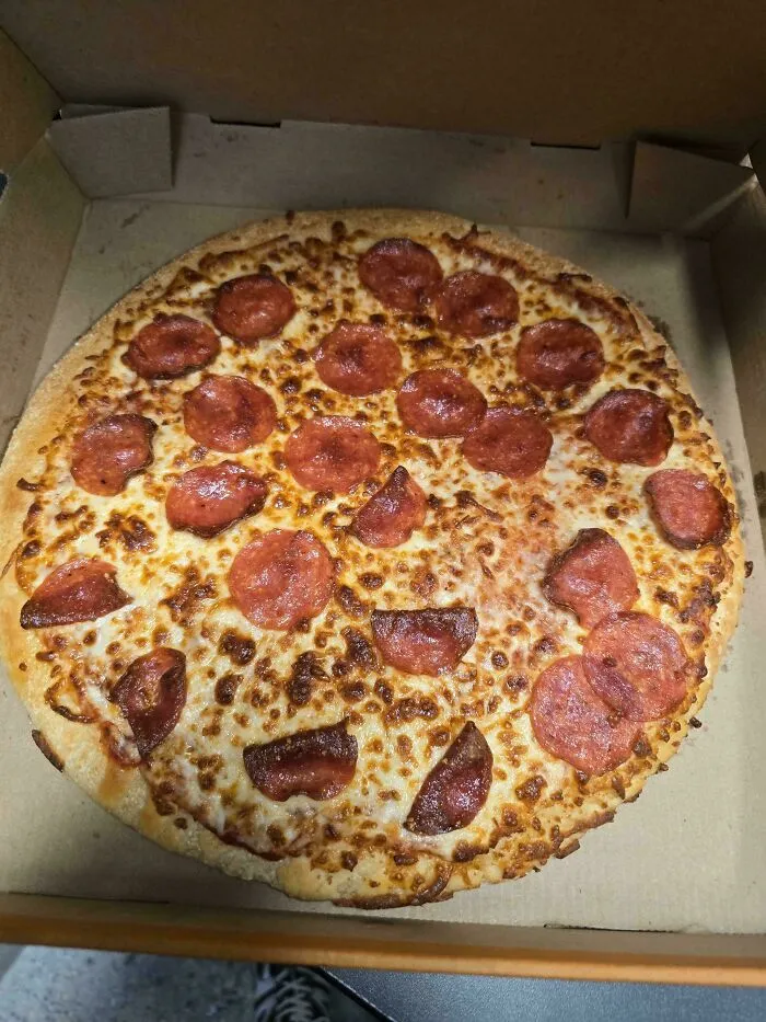 Pepperoni pizza with unevenly placed toppings in a box, showing a funny unfortunate situation of forgotten pizza preparation.