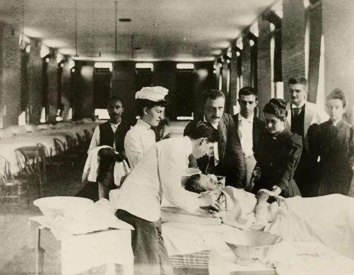 Vintage photo of nurses and doctors caring for a patient in a hospital ward, showcasing early nursing and healing efforts.