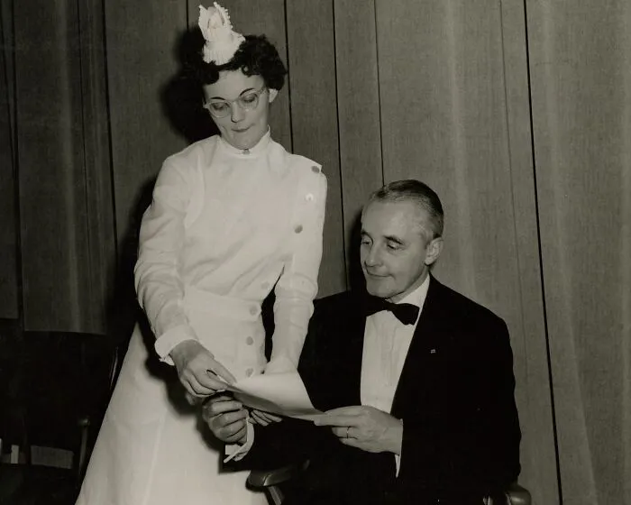 Vintage photo of a nurse in traditional uniform assisting a man in a suit, showcasing healing and hope in nursing history.
