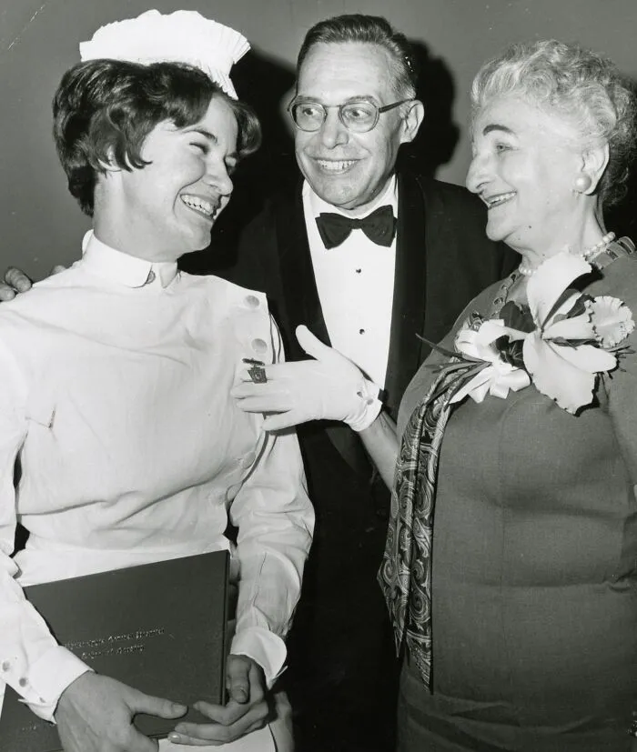Vintage photo of a nurse smiling with two people at a formal event, showcasing classic nurse healing and hope.