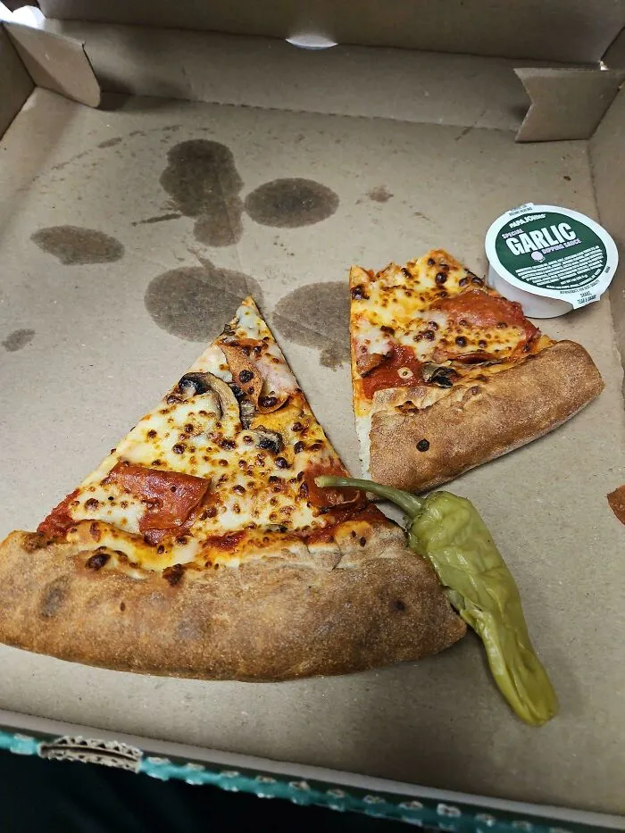 Dos rebanadas de pizza en caja con salsa de ajo y chile, ejemplo de personas que llevan un día peor en el trabajo que tú.